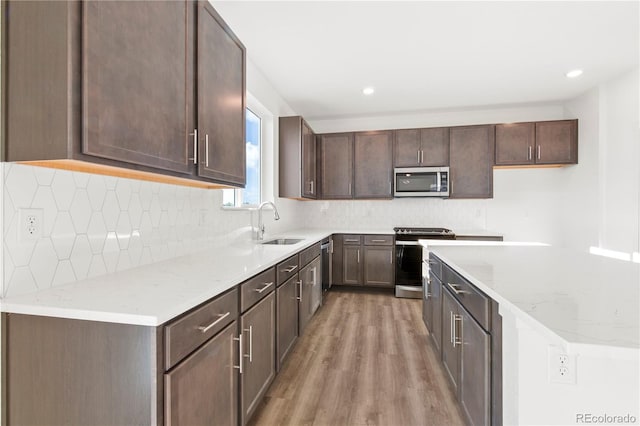 kitchen featuring sink, light stone countertops, light wood-type flooring, dark brown cabinets, and stainless steel appliances