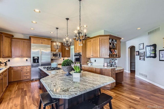 kitchen with built in appliances, arched walkways, a chandelier, a kitchen bar, and recessed lighting