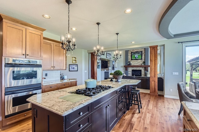kitchen featuring stainless steel double oven, a chandelier, black gas stovetop, a kitchen island, and light wood-type flooring