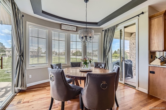 dining room featuring a chandelier, light wood-type flooring, baseboards, and a raised ceiling