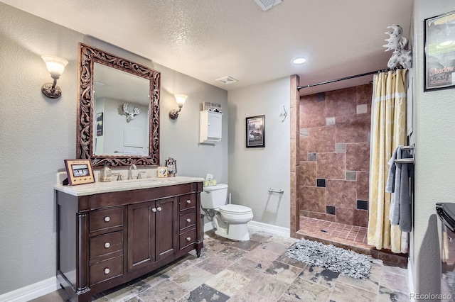 bathroom featuring toilet, tiled shower, vanity, baseboards, and a textured ceiling