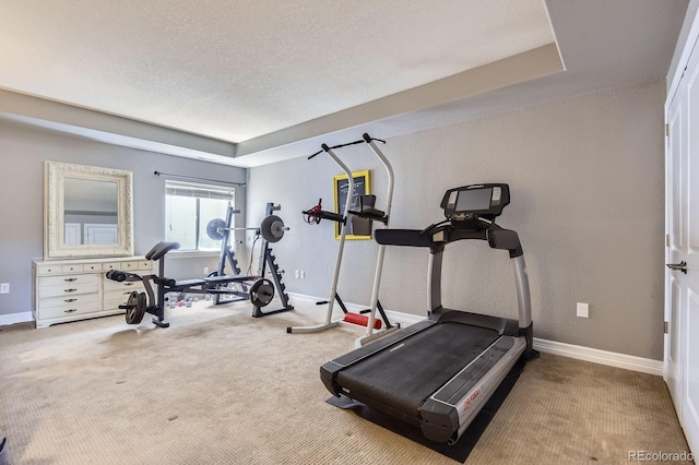 workout room featuring carpet floors, baseboards, a textured ceiling, and a tray ceiling