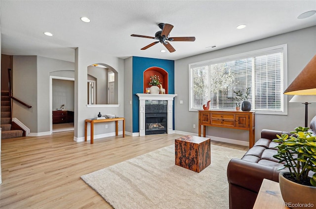 living room featuring a tiled fireplace, stairs, ceiling fan, and wood finished floors