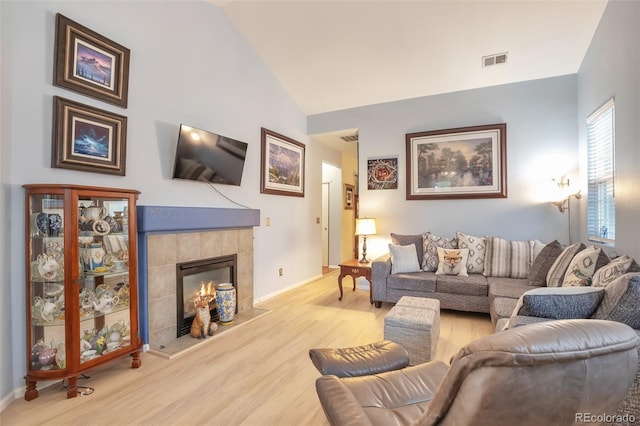 living area with wood finished floors, a tiled fireplace, baseboards, and high vaulted ceiling