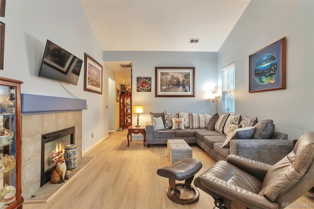 living room featuring light wood-type flooring, a tiled fireplace, lofted ceiling, and baseboards