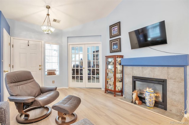 sitting room with wood finished floors, french doors, a tile fireplace, baseboards, and vaulted ceiling