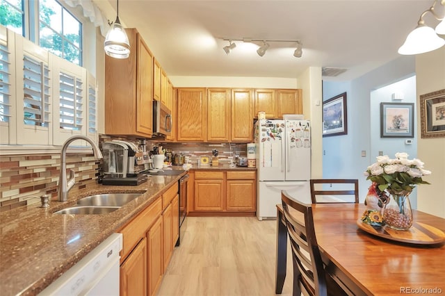 kitchen featuring appliances with stainless steel finishes, a sink, decorative backsplash, dark stone counters, and light wood-type flooring