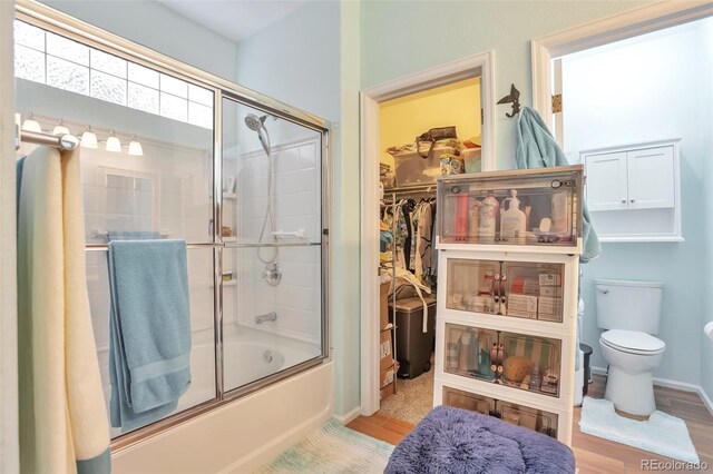 bathroom with shower / bath combination with glass door, toilet, wood finished floors, baseboards, and a walk in closet
