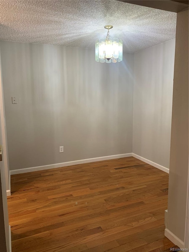 empty room featuring an inviting chandelier, a textured ceiling, and hardwood / wood-style flooring