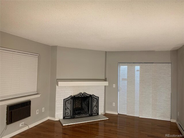 unfurnished living room featuring a baseboard heating unit, a textured ceiling, dark hardwood / wood-style floors, an AC wall unit, and a brick fireplace