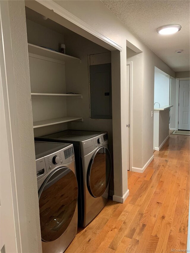 laundry area featuring light hardwood / wood-style floors, a textured ceiling, washing machine and dryer, and electric panel