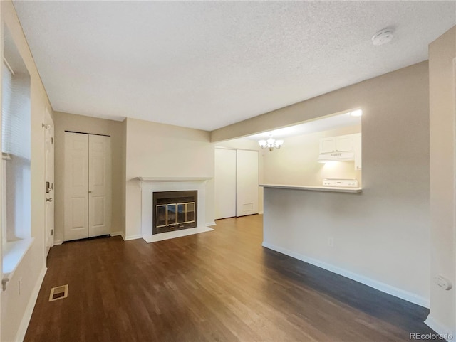 unfurnished living room featuring a notable chandelier, dark hardwood / wood-style floors, and a textured ceiling