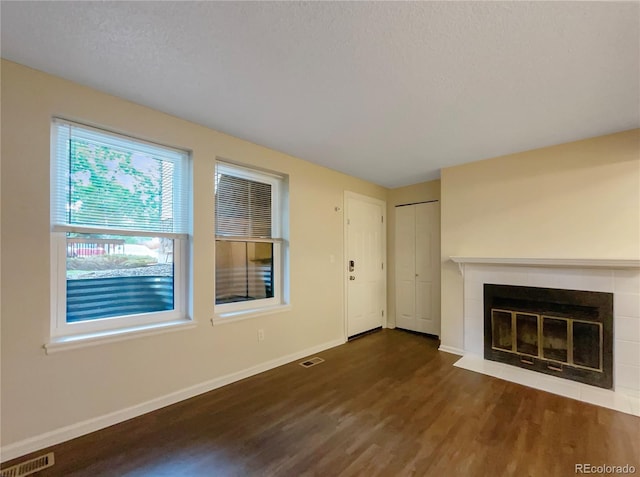 unfurnished living room with a tile fireplace, dark wood-type flooring, and a textured ceiling