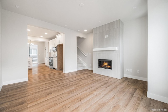 unfurnished living room with light wood-type flooring, a chandelier, and a fireplace