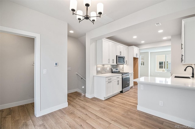 kitchen with sink, light wood-type flooring, white cabinetry, pendant lighting, and stainless steel appliances