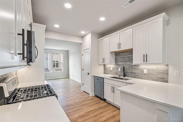 kitchen with appliances with stainless steel finishes, sink, light hardwood / wood-style flooring, white cabinetry, and tasteful backsplash