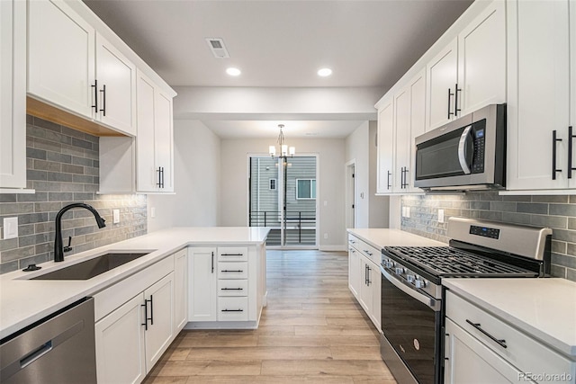 kitchen with white cabinetry, hanging light fixtures, stainless steel appliances, light hardwood / wood-style flooring, and sink