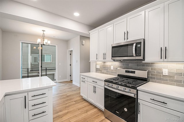 kitchen featuring hanging light fixtures, stainless steel appliances, white cabinets, decorative backsplash, and light wood-type flooring