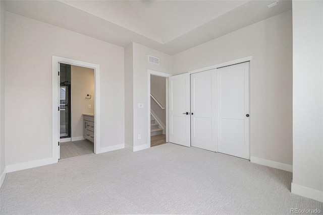 unfurnished bedroom with light carpet, ensuite bath, and a closet