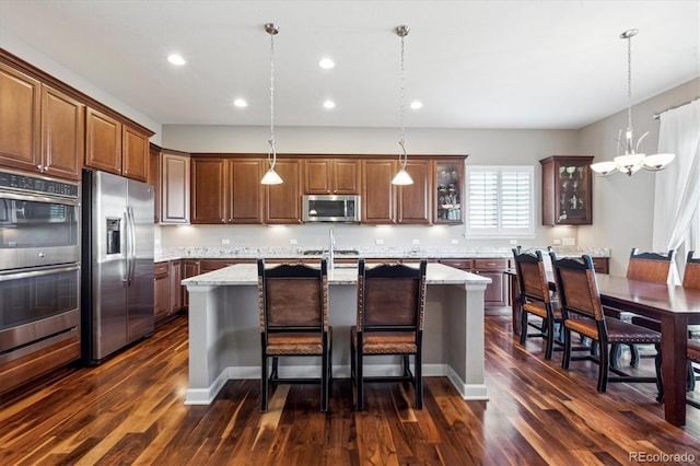 kitchen featuring light stone countertops, appliances with stainless steel finishes, a kitchen island with sink, and pendant lighting