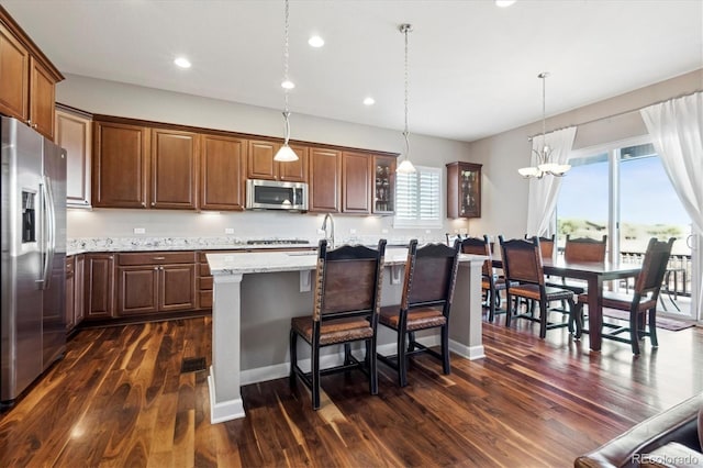 kitchen featuring pendant lighting, a center island with sink, dark hardwood / wood-style floors, light stone countertops, and stainless steel appliances