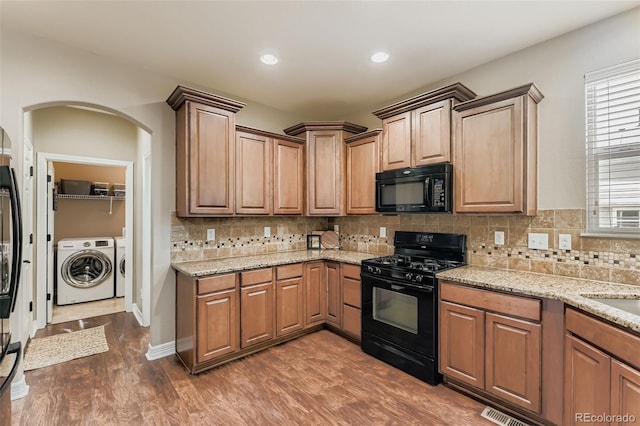 12763 E 105th Pl, Commerce City, CO 80022 - kitchen featuring black appliances, washer and clothes dryer, arched walkways, dark wood-style floors, and light stone countertops