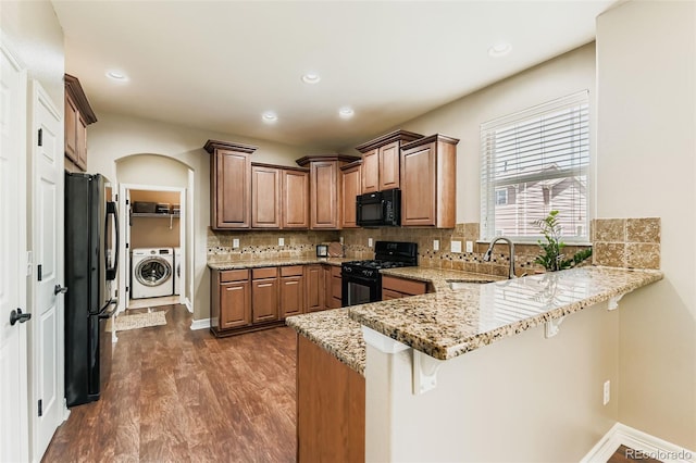 12763 E 105th Pl, Commerce City, CO 80022 - kitchen featuring washer / clothes dryer, black appliances, a peninsula, dark wood-style floors, and a breakfast bar