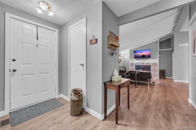 foyer with vaulted ceiling, light wood-type flooring, a textured ceiling, and a tile fireplace