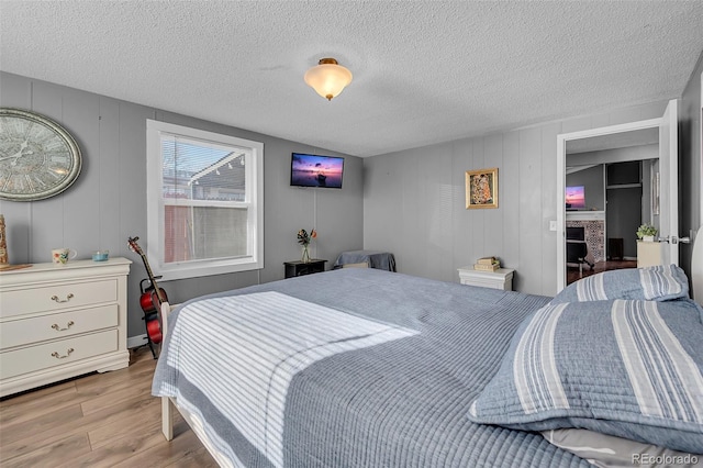 bedroom with a textured ceiling, wood walls, and light hardwood / wood-style flooring