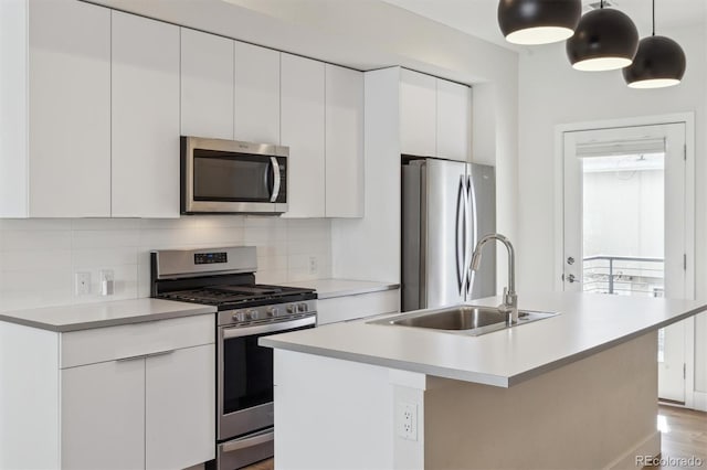 kitchen with a kitchen island with sink, stainless steel appliances, a sink, white cabinets, and backsplash