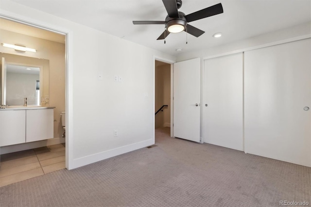 unfurnished bedroom featuring a closet, light colored carpet, visible vents, light tile patterned flooring, and ensuite bath