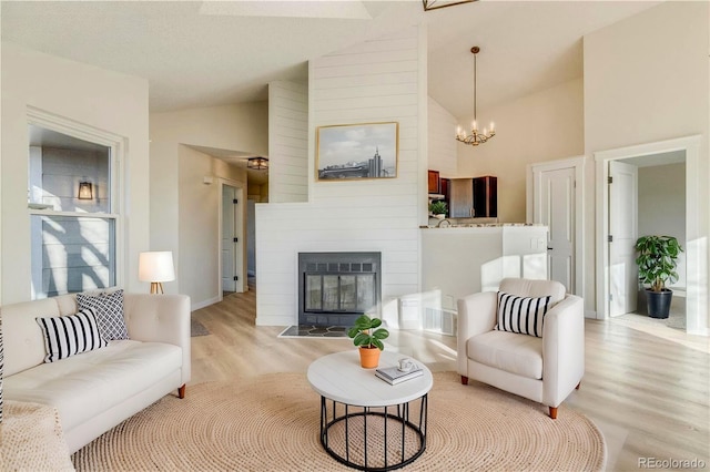 living room featuring a notable chandelier, a fireplace, high vaulted ceiling, and light hardwood / wood-style flooring