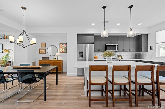 kitchen featuring tasteful backsplash, light wood-style flooring, light countertops, dark cabinetry, and stainless steel appliances