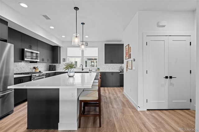 kitchen featuring light countertops, appliances with stainless steel finishes, light wood-style floors, dark cabinets, and a kitchen island
