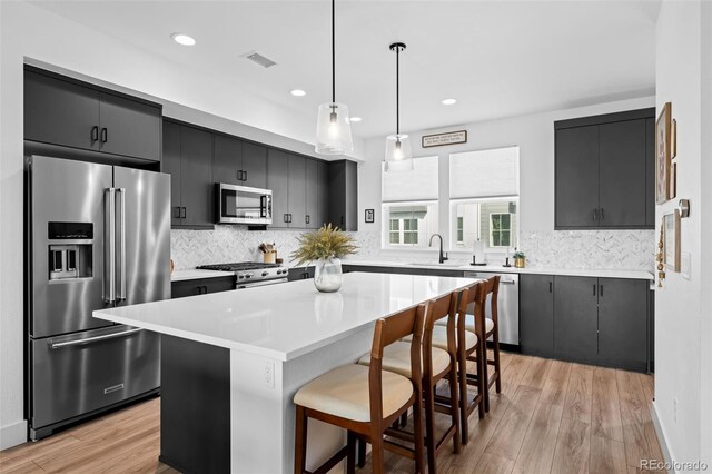 kitchen featuring a center island, appliances with stainless steel finishes, a sink, hanging light fixtures, and backsplash