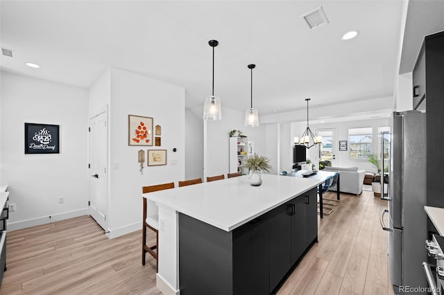 kitchen with dark cabinets, light wood-style flooring, a kitchen breakfast bar, and freestanding refrigerator