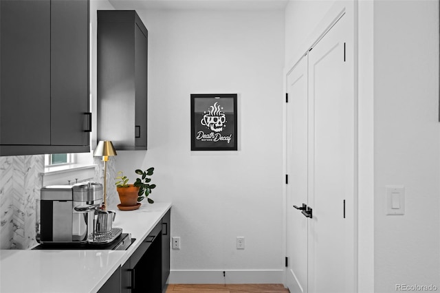 kitchen featuring dark cabinets, wood finished floors, light countertops, and baseboards