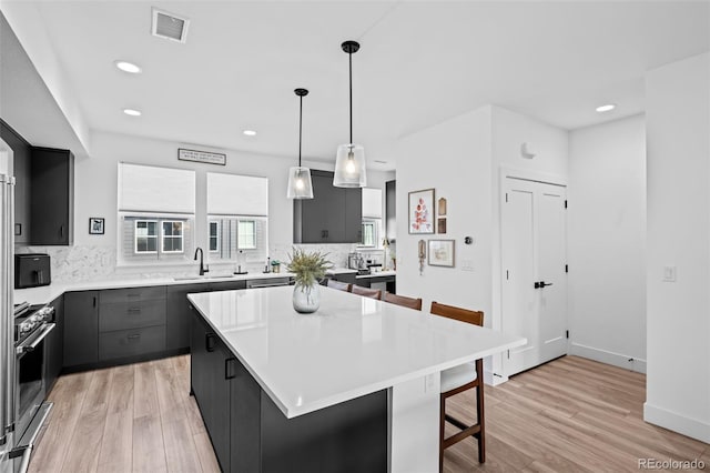 kitchen featuring light wood-style flooring, a kitchen bar, light countertops, and stainless steel range oven