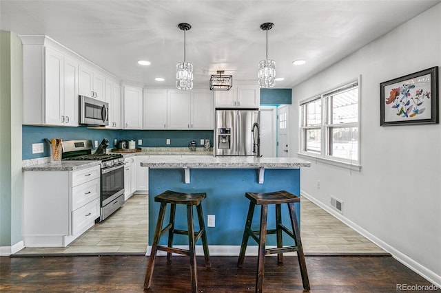 kitchen with stainless steel appliances, white cabinets, a kitchen bar, an island with sink, and hanging light fixtures