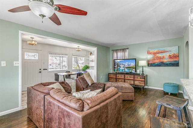 living room featuring ceiling fan, built in shelves, and dark wood-type flooring