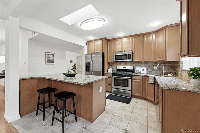 981 Ursula St, Aurora, CO 80011 - kitchen with appliances with stainless steel finishes, a kitchen bar, light stone countertops, tasteful backsplash, and a peninsula