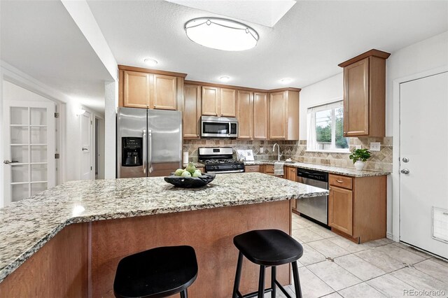 981 Ursula St, Aurora, CO 80011 - kitchen featuring appliances with stainless steel finishes, a breakfast bar area, light stone countertops, decorative backsplash, and light tile patterned flooring