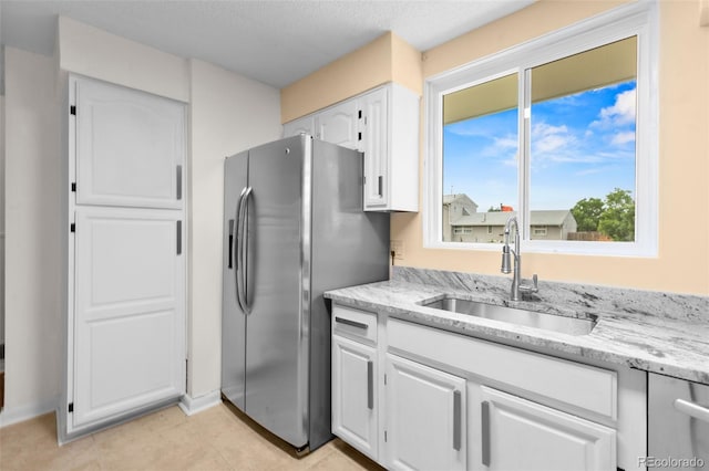600 Bronco Rd, Denver, CO 80221 - kitchen with stainless steel fridge, white cabinets, light stone counters, and light tile patterned floors