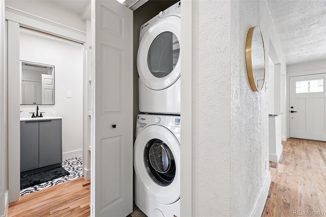 3344 W 33rd Ave, Denver, CO 80211 - laundry area featuring stacked washing machine and dryer, light wood-type flooring, a textured wall, a textured ceiling, and baseboards