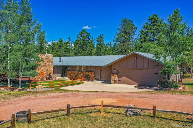 view of front of property featuring a garage, dirt driveway, stone siding, metal roof, and board and batten siding