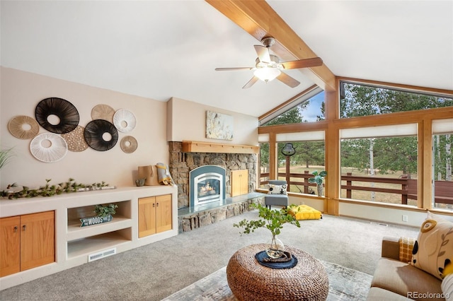 carpeted living room featuring lofted ceiling with beams, a stone fireplace, and ceiling fan