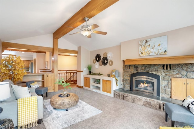 carpeted living room featuring lofted ceiling with beams, ceiling fan, a stone fireplace, and baseboards