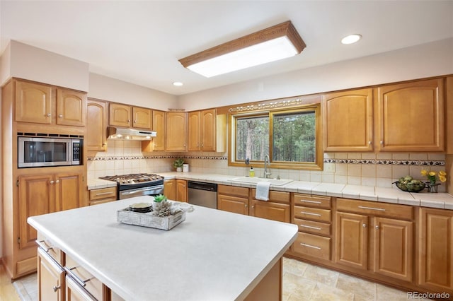 kitchen featuring under cabinet range hood, a sink, light countertops, appliances with stainless steel finishes, and a center island