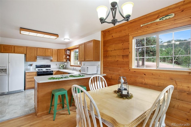 dining area with wood walls, a notable chandelier, light hardwood / wood-style floors, and sink