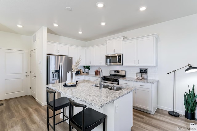 kitchen with appliances with stainless steel finishes, light wood-type flooring, a sink, and decorative backsplash